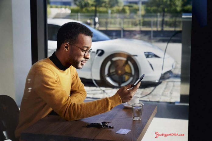 African American man with his Taycan charging in bg. Credit: PCNA Porsche launches Porsche Finder, its pre-owned vehicle search platform - Pictured here is an African American man operating his smartphone, with his Taycan charging in b.g. Credit: PCNA